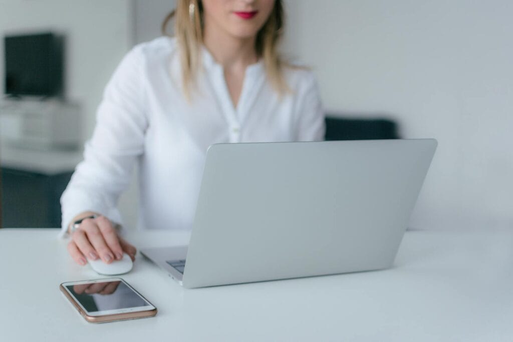 Assistente Home Office Sem Experiência A woman working at a desk using a laptop and smartphone, exemplifying remote work.