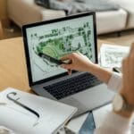 10 Vagas de Emprego na Qualidados Architect reviewing landscape design on laptop, enhancing architectural projects from home office.