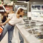 Vagas de Emprego no Assaí Focused young woman in casual wear picking food from showcase fridge and holding grocery basket while buying products in modern supermarket